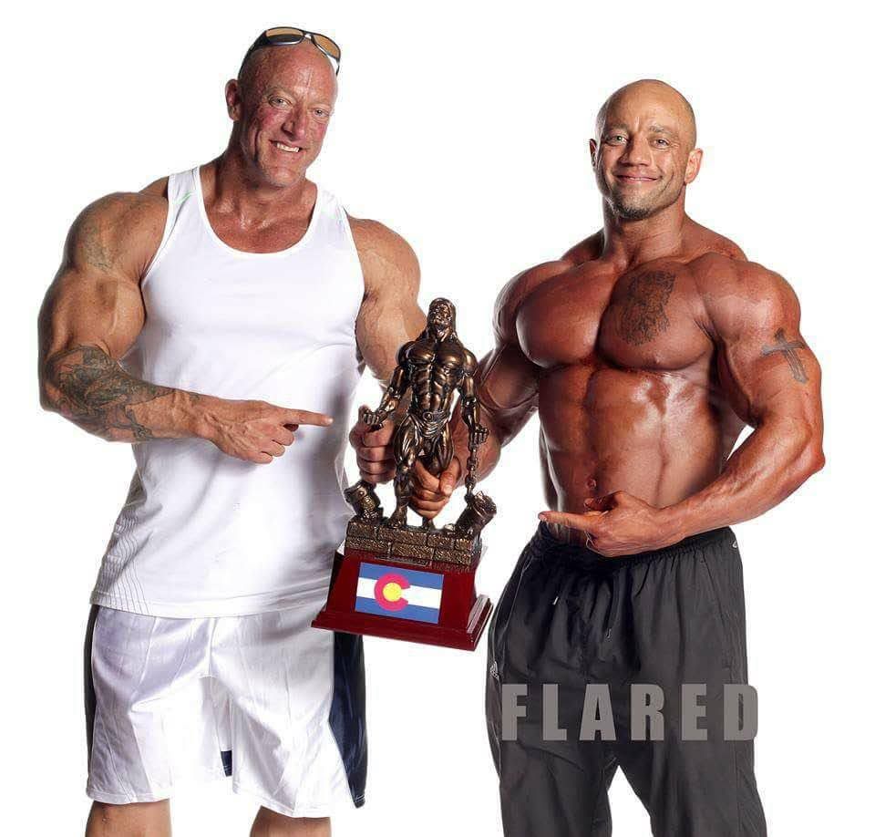 Two muscular men standing next to each other holding a trophy that says flared