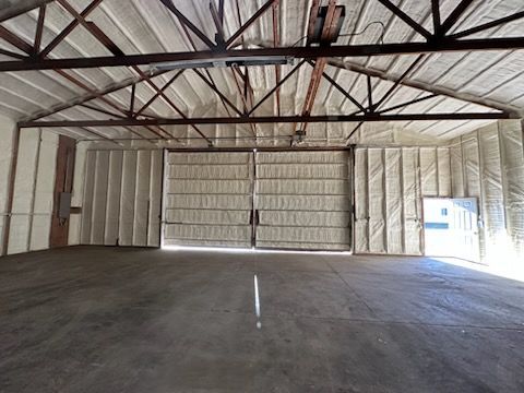 Interior view of an industrial building insulated with spray foam. Open doors at the far end; concrete floor.