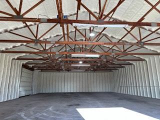 Interior of a large warehouse with spray foam insulation on the walls and ceiling, exposed wooden beams, and concrete floor.
