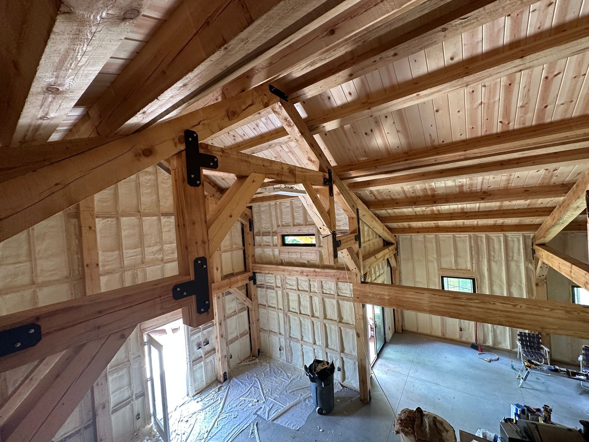 Interior of a room under construction with exposed wooden framing and insulation. Window and open loft area.