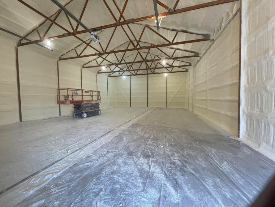 Interior of a large building with spray foam insulation on the walls and ceiling. A lift sits in the center.