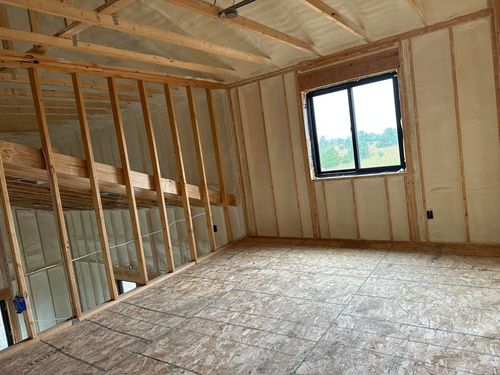 Interior of a room under construction with exposed wooden framing and insulation. Window and open loft area.