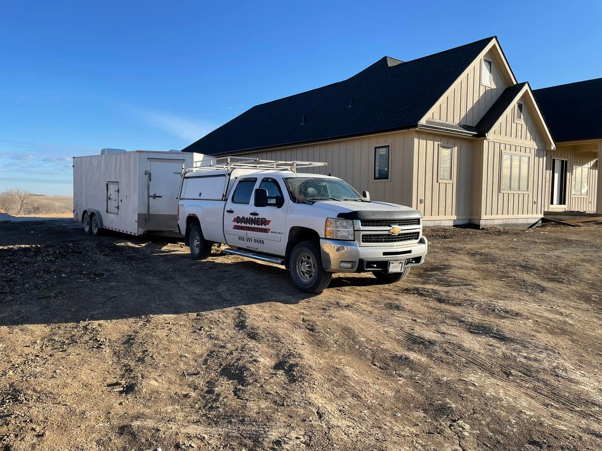 White truck pulling a trailer parked in front of a house under construction on a sunny day.