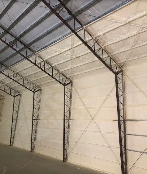 Interior of a large building with exposed steel beams and white insulated walls.