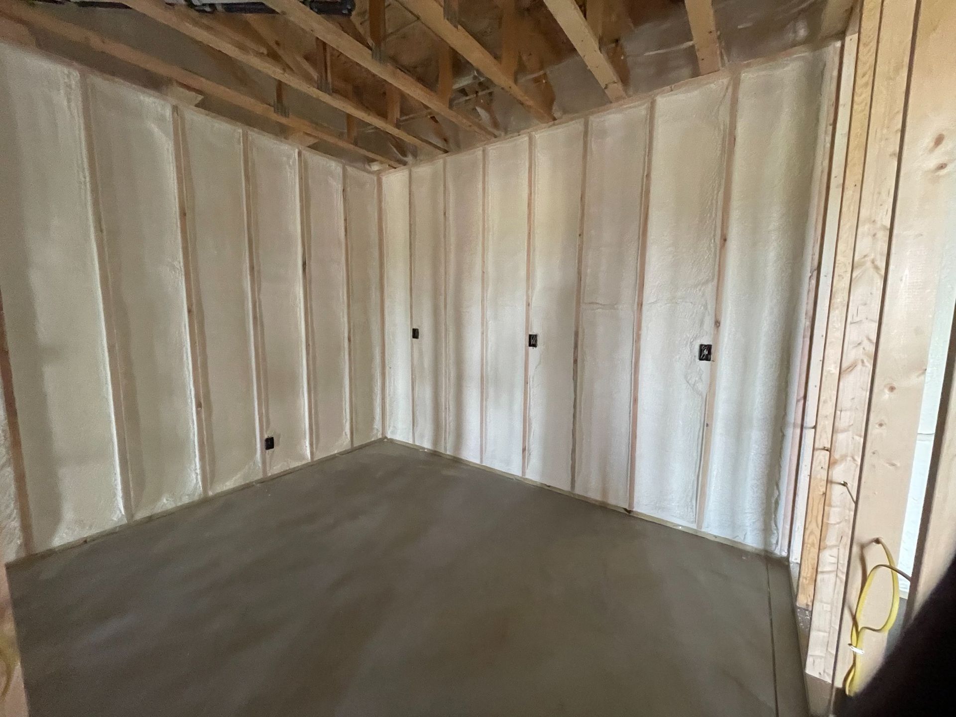 Interior room under construction, with spray foam insulation on the walls and a concrete floor.