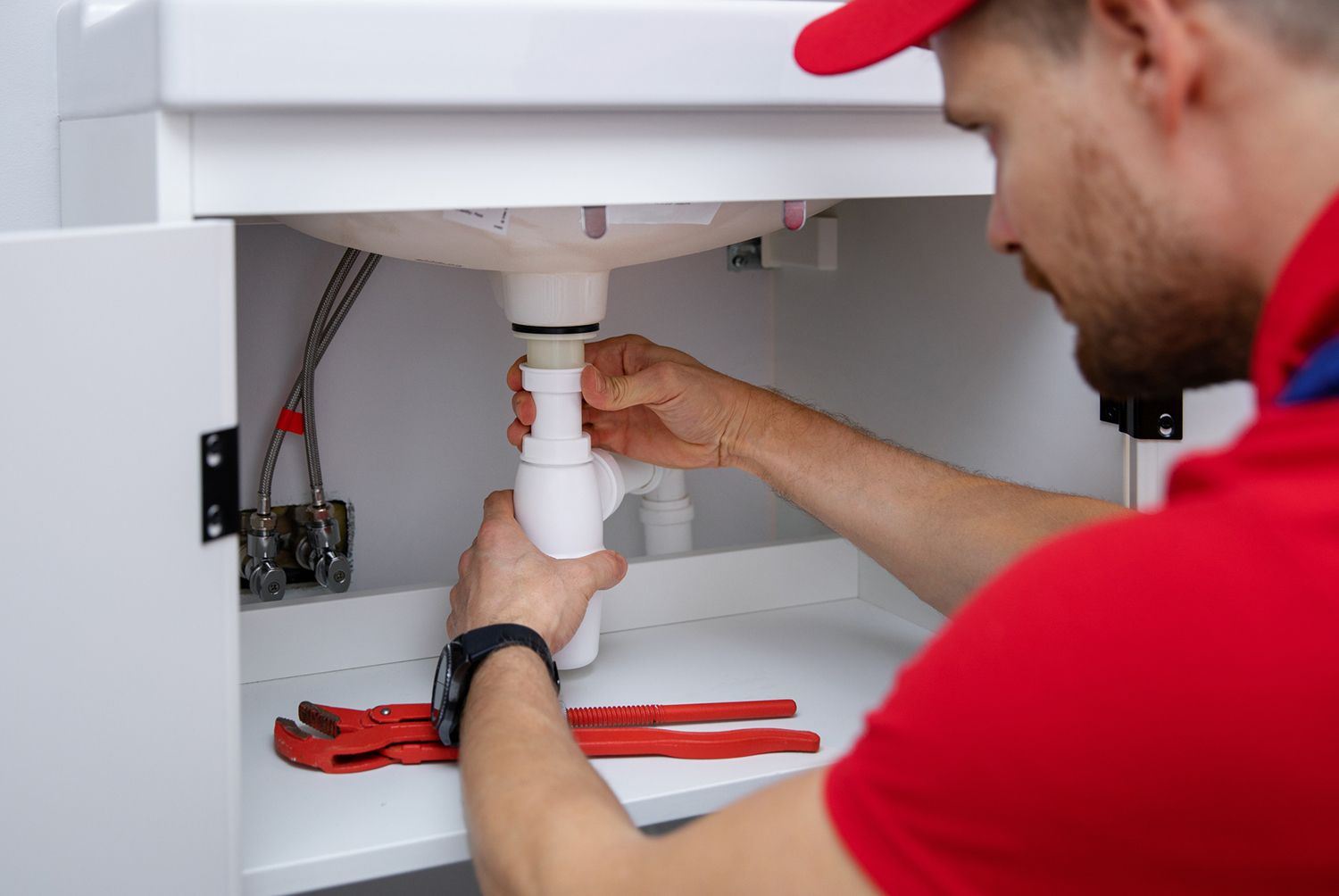 Plumber fixing sink drain pipe under cabinet with professional plumbing tools.