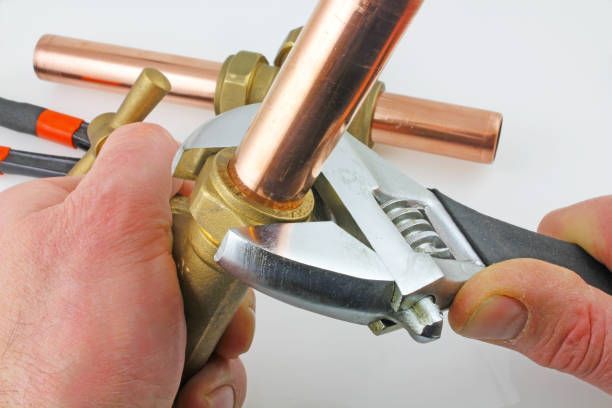 Close-up of the hands of a plumber as he tightens the compression on a copper pipe with a wrench.