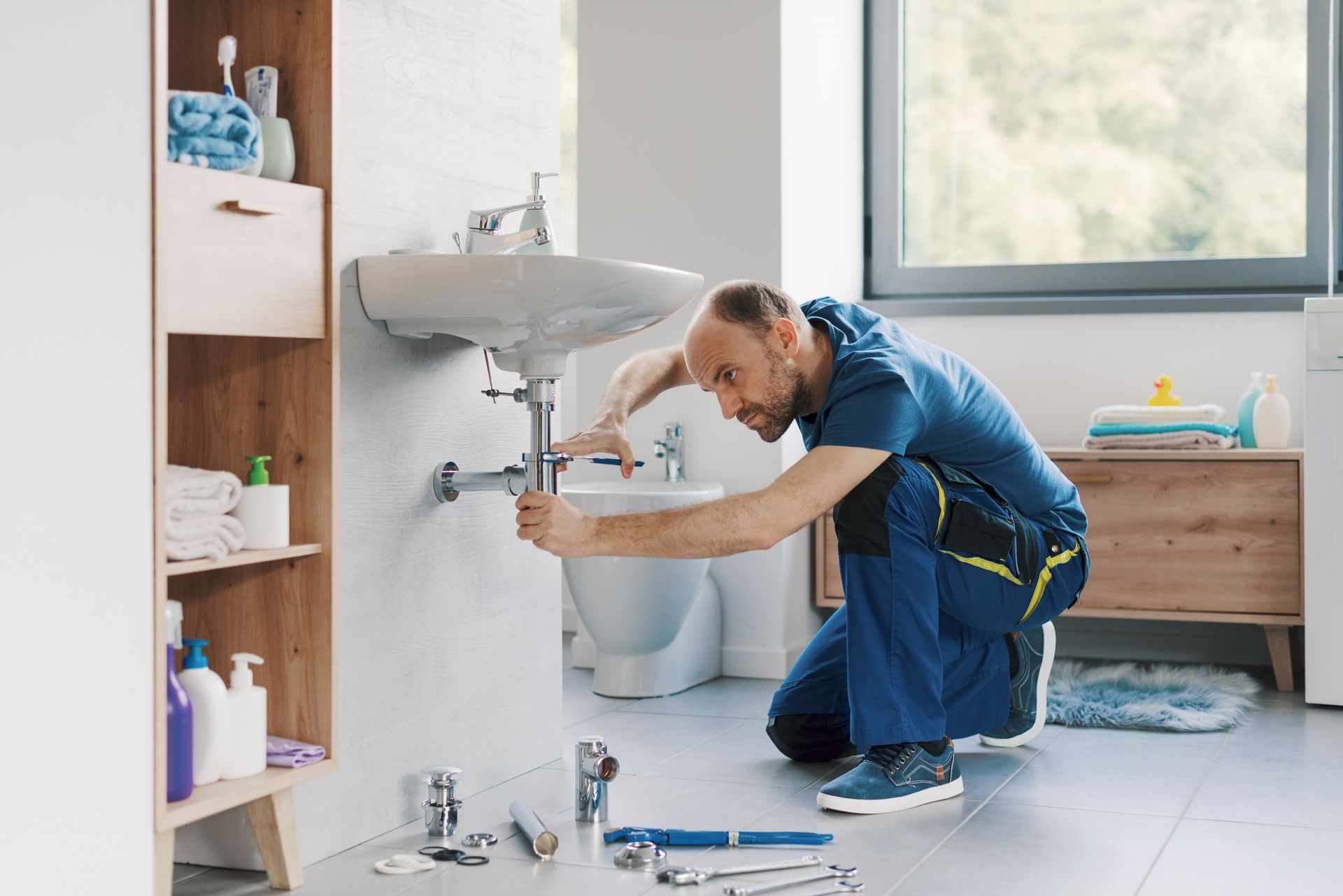 Professional plumber installing a bathroom sink and pipes, using water pump pliers.