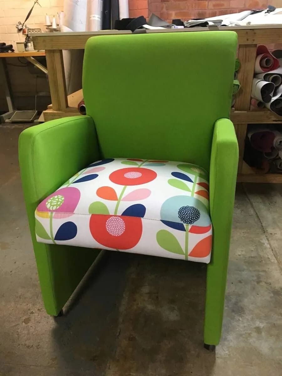 A green chair with a colourful floral cushion is sitting on a concrete floor — Metreson Upholstery In Unanderra, NSW