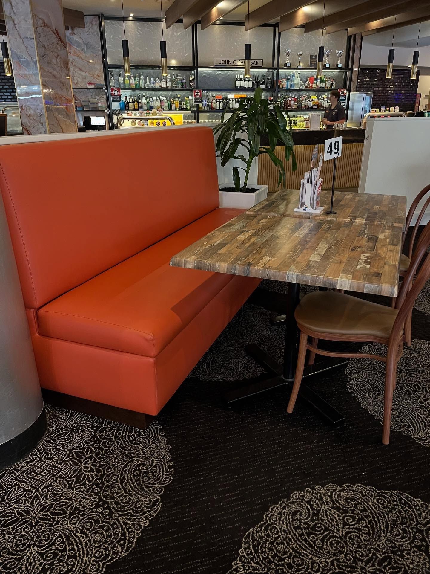 Orange booth seating with a textured wooden table and a wooden chair in a restaurant setting.— Metreson Upholstery In Unanderra, NSW