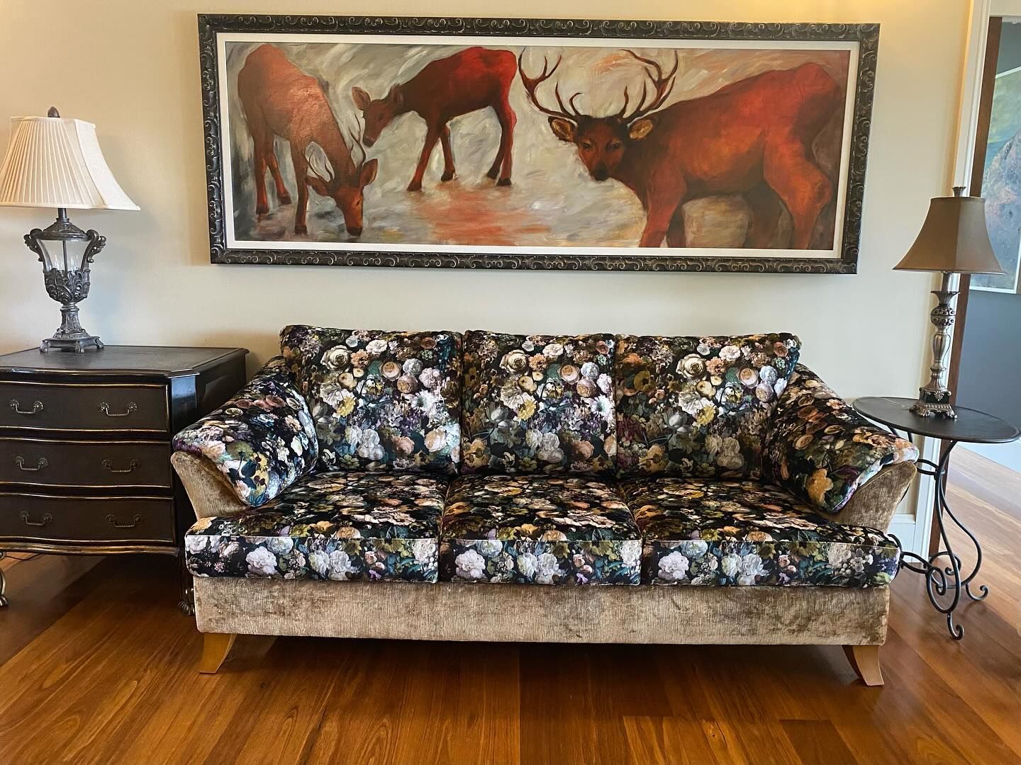 Sofa with floral pattern in front of a painting of three deer, flanked by lamps and tables. — Metreson Upholstery In Unanderra, NSW