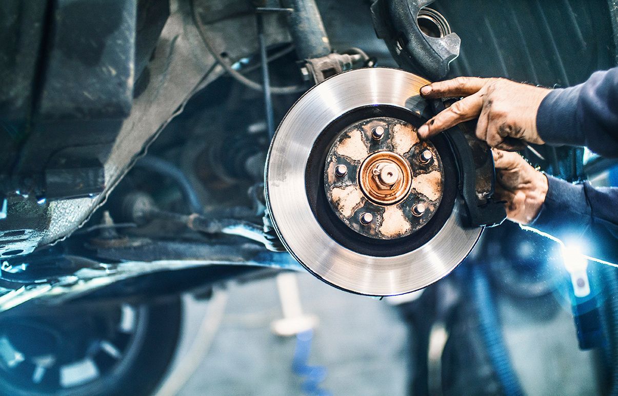 A man is fixing a brake disc on a car in a garage.