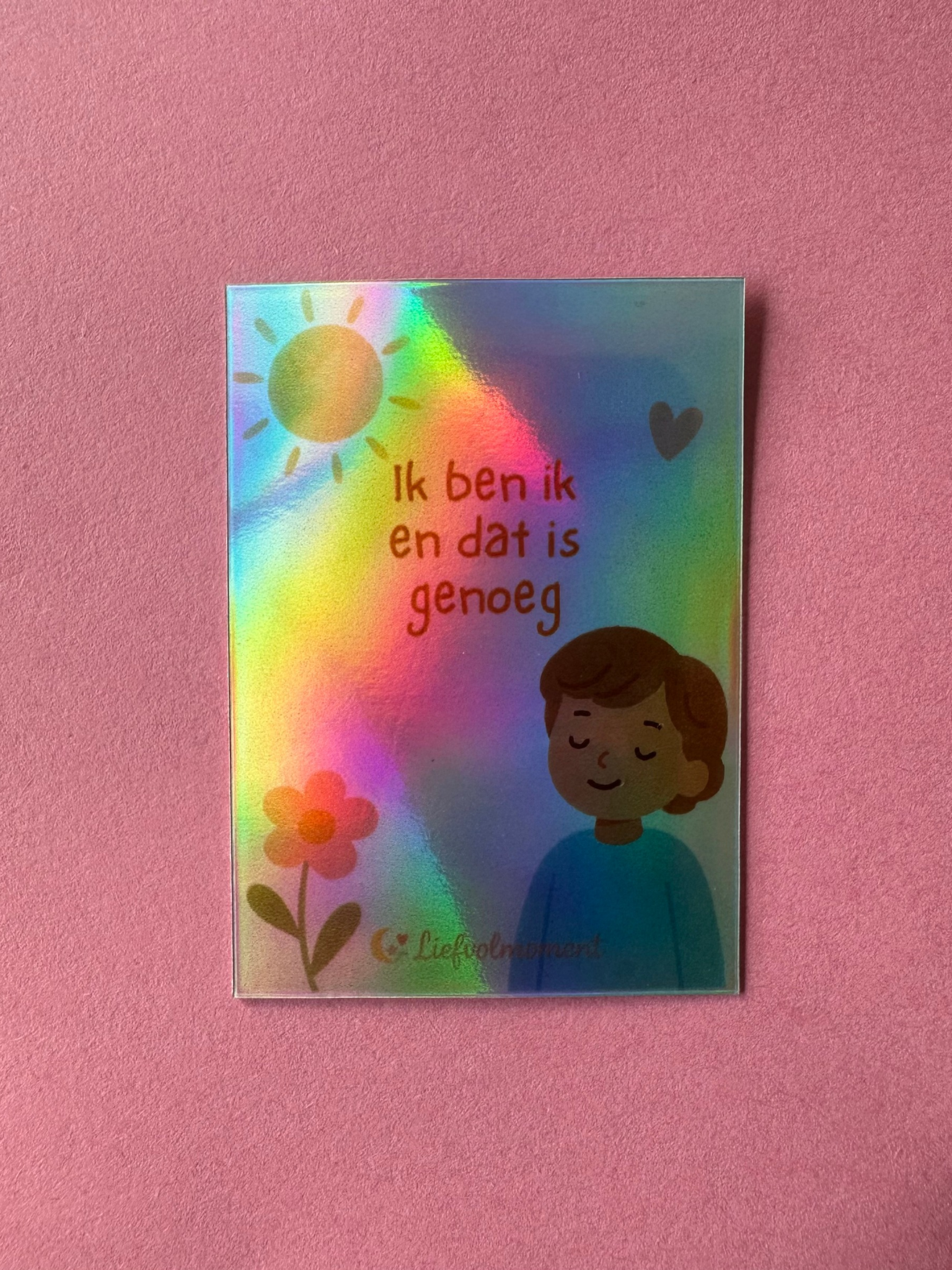 Holographic card showing a sun, a flower, a smiling figure, and the Dutch text:
