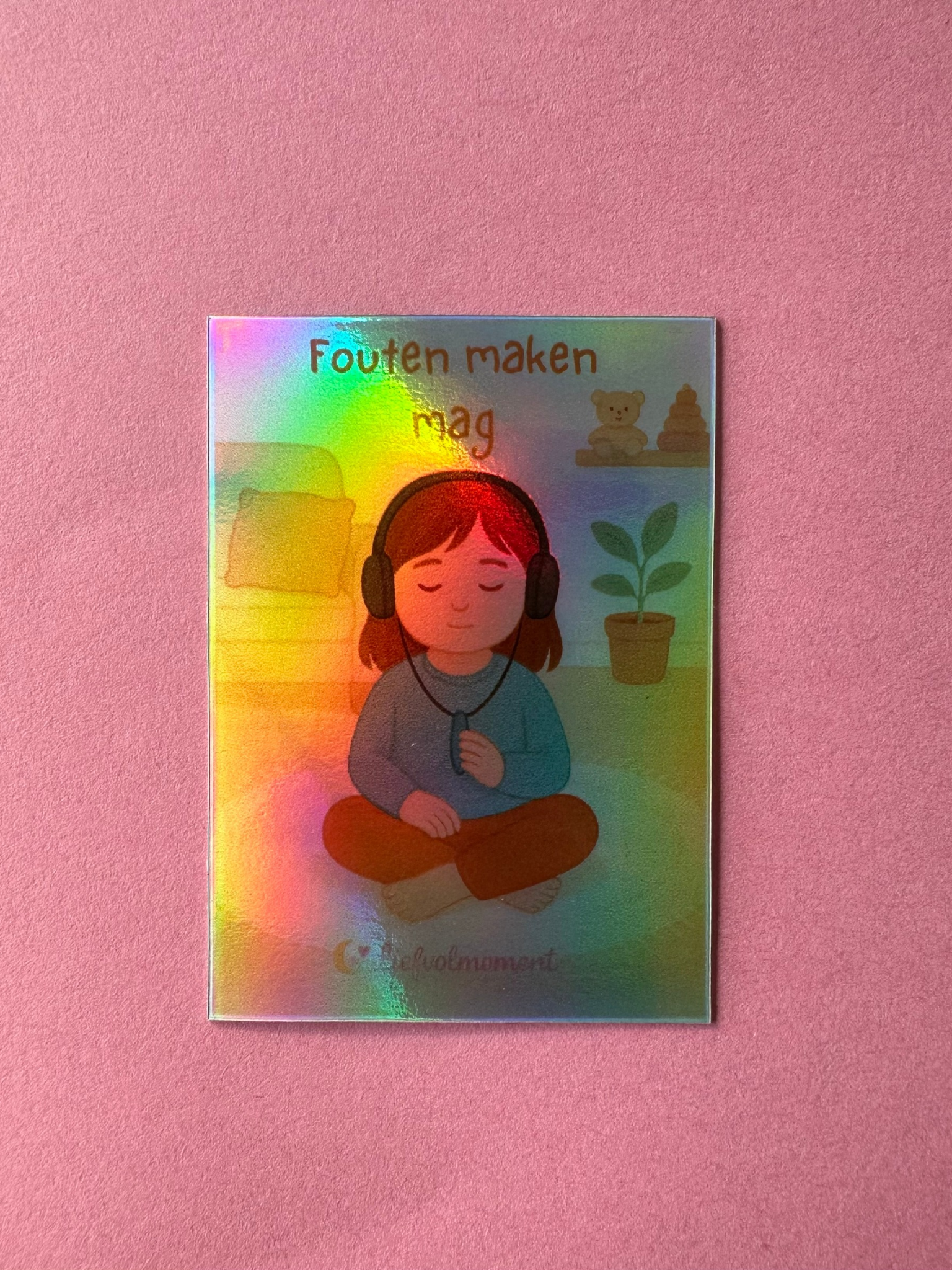 Een holografische sticker toont een persoon die mediteert met een koptelefoon op. De tekst erboven luidt