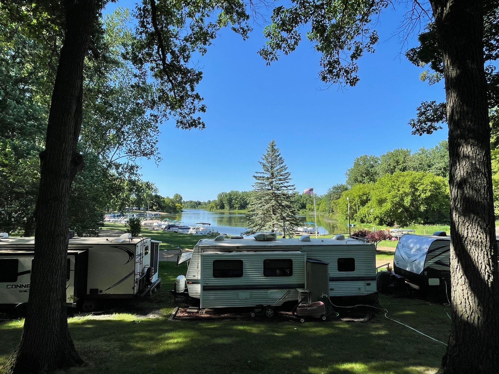 A rv parked in a grassy area with trees and a lake in the background