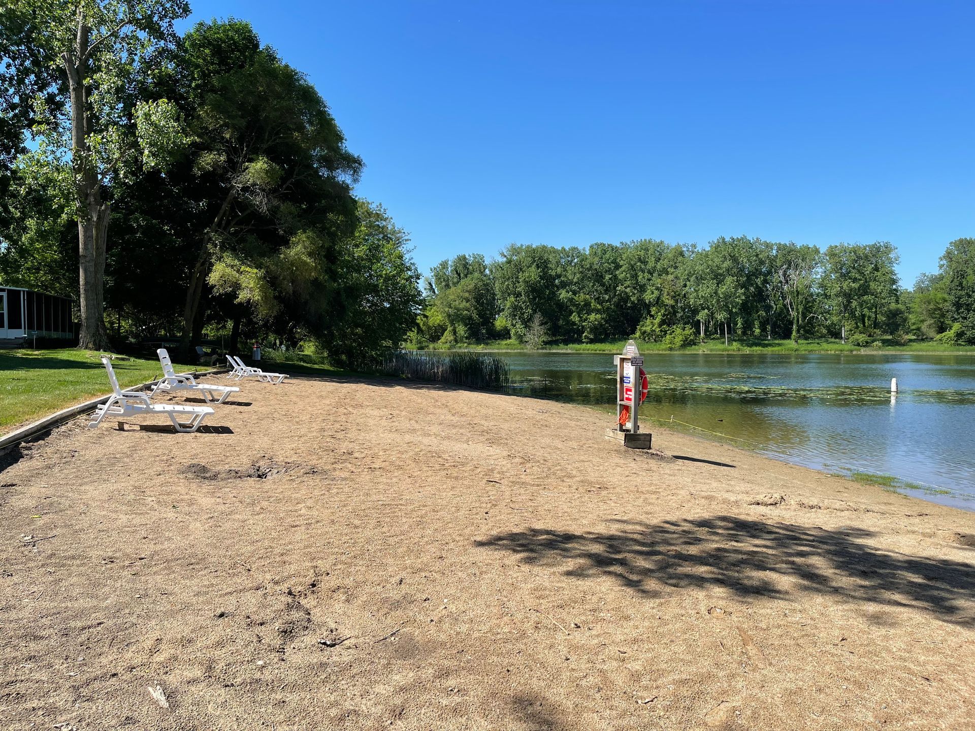 A sandy beach next to a lake with chairs and trees.