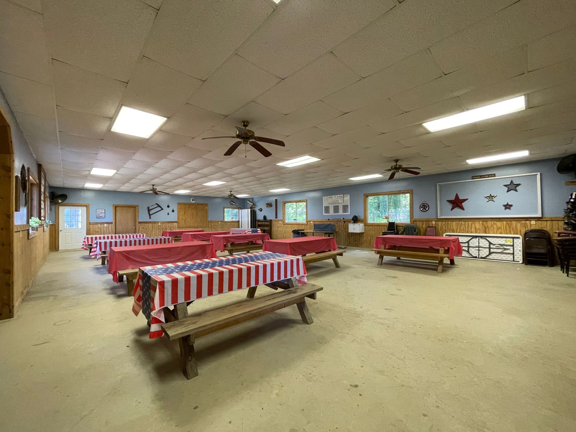A large room with tables and benches and a ceiling fan.