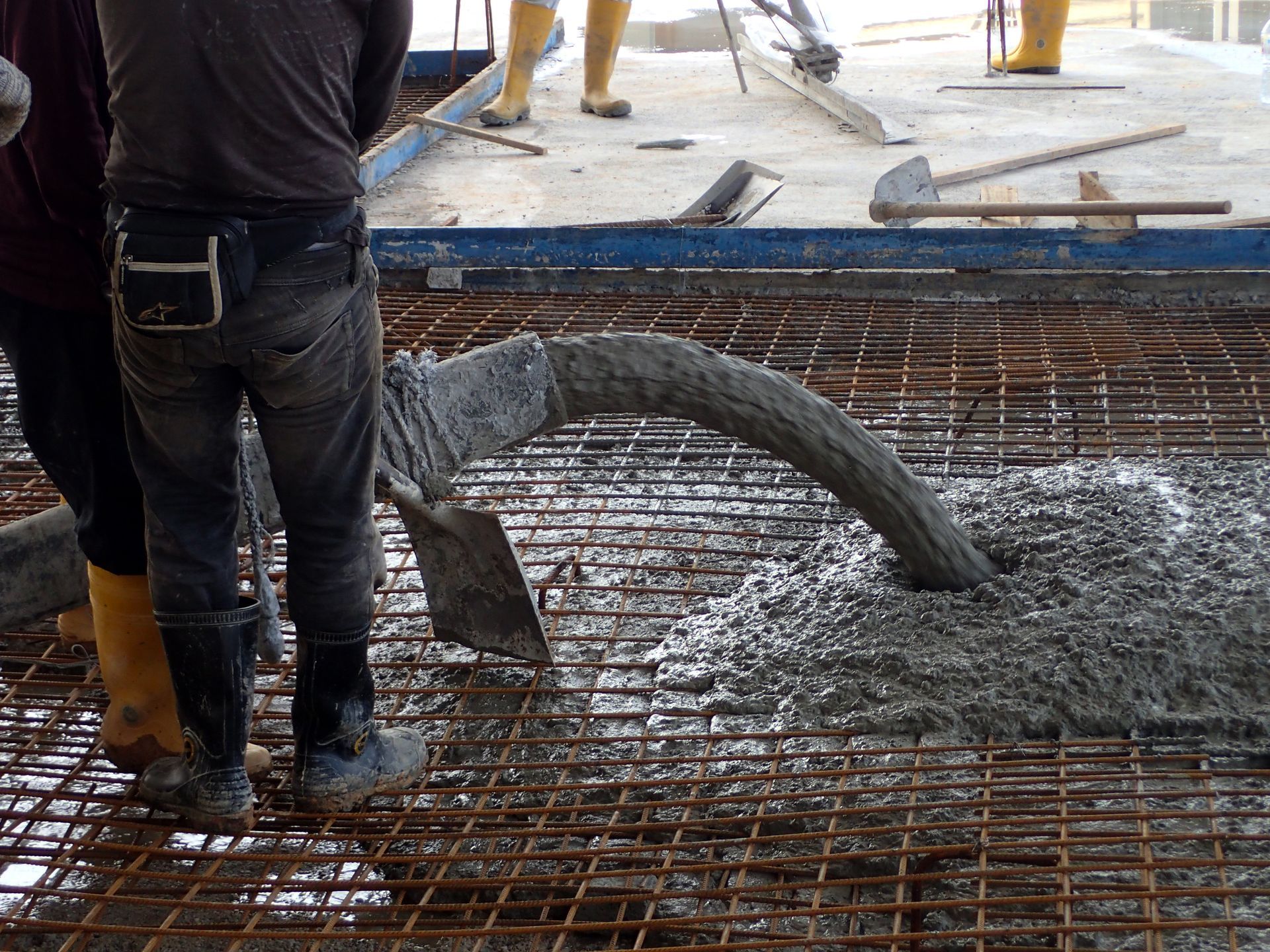 A man is pouring concrete into a grid on a construction site.