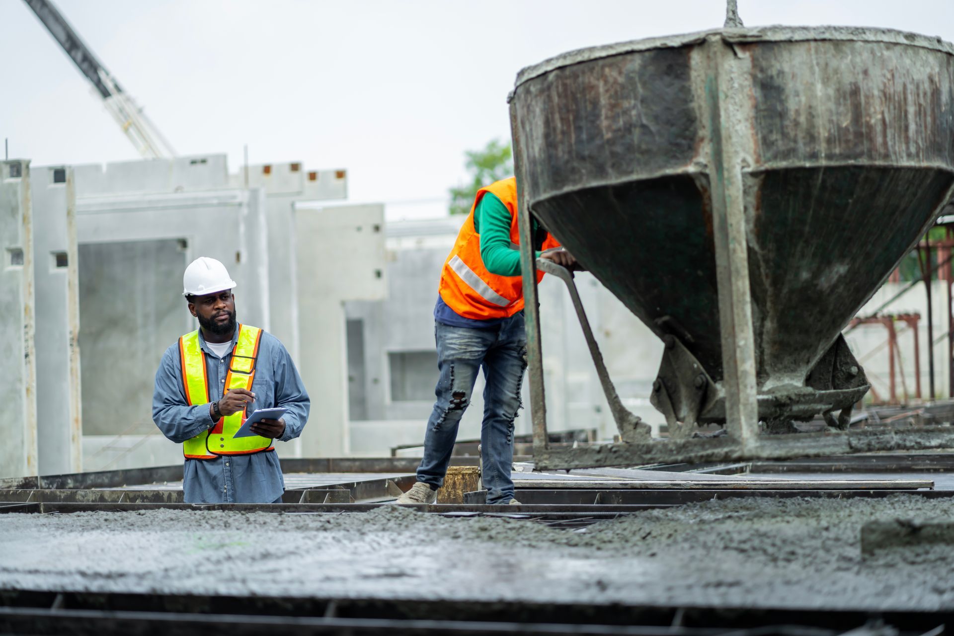 Two construction workers are working on a concrete floor at a construction site.