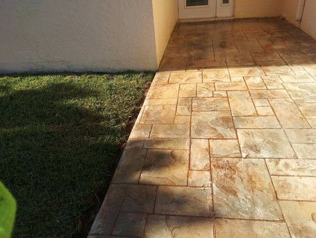 A concrete walkway leading to a house next to a grassy area.