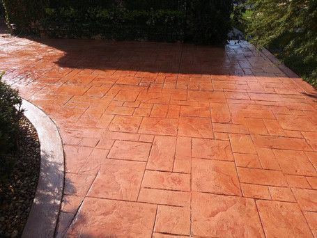 A concrete driveway with a brick pattern is surrounded by trees and bushes.