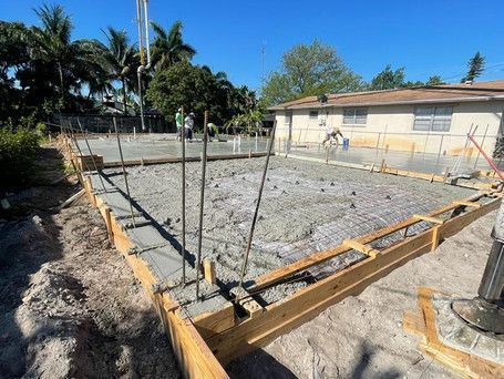 A concrete base for a house is being poured in front of a house.