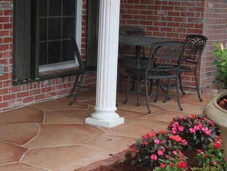 A patio with a table and chairs and flowers in front of a brick building.