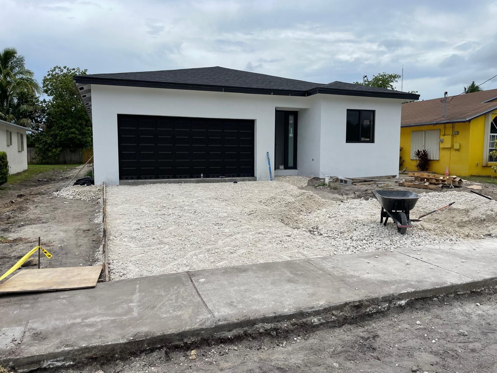 A white house with a black garage door and a wheelbarrow in front of it.