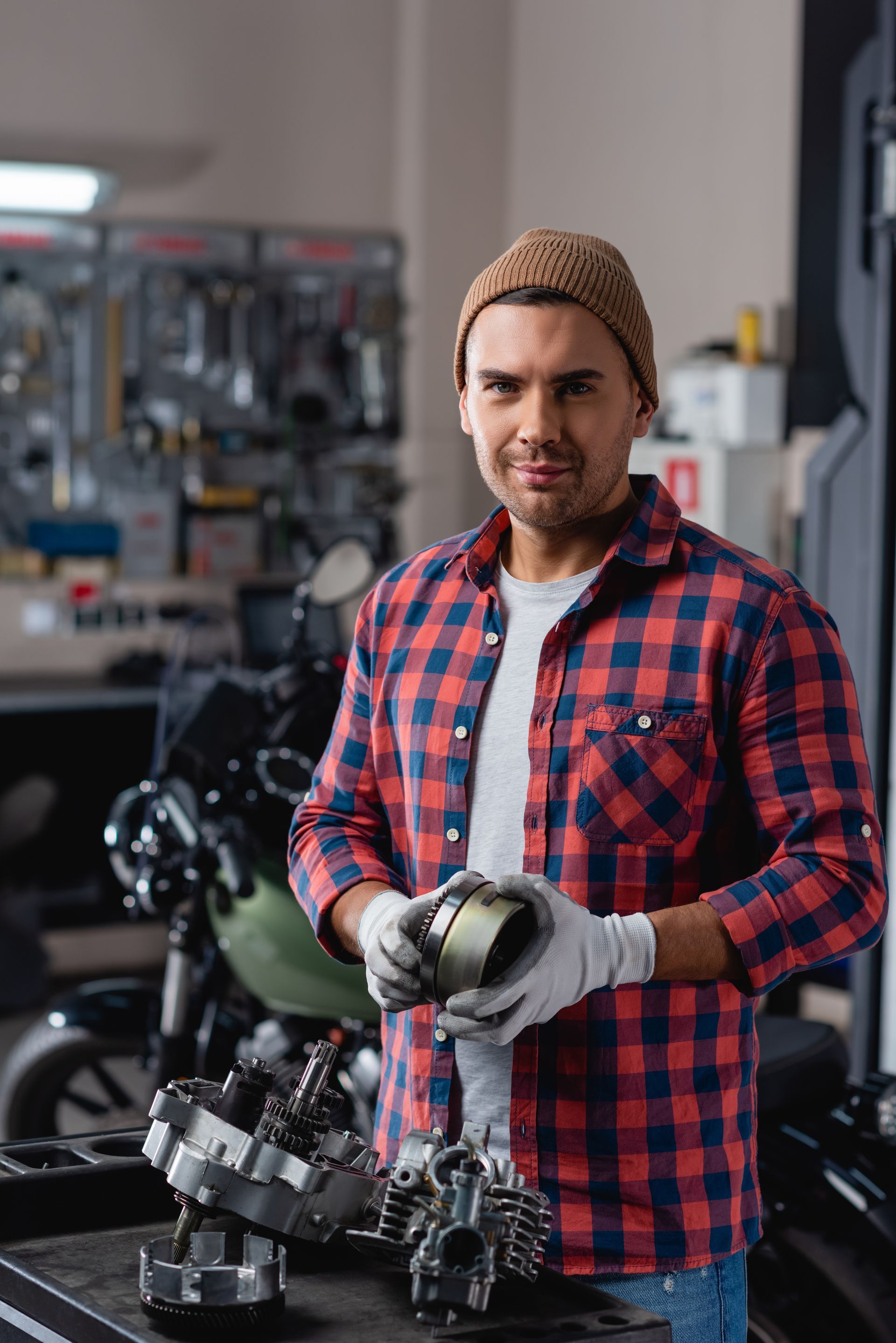 A man in a plaid shirt is working on a motorcycle in a garage.