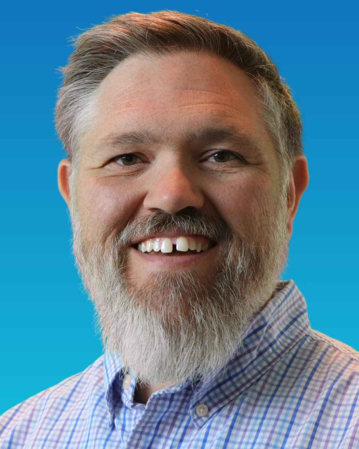 A man with a beard is wearing a plaid shirt and a microphone.