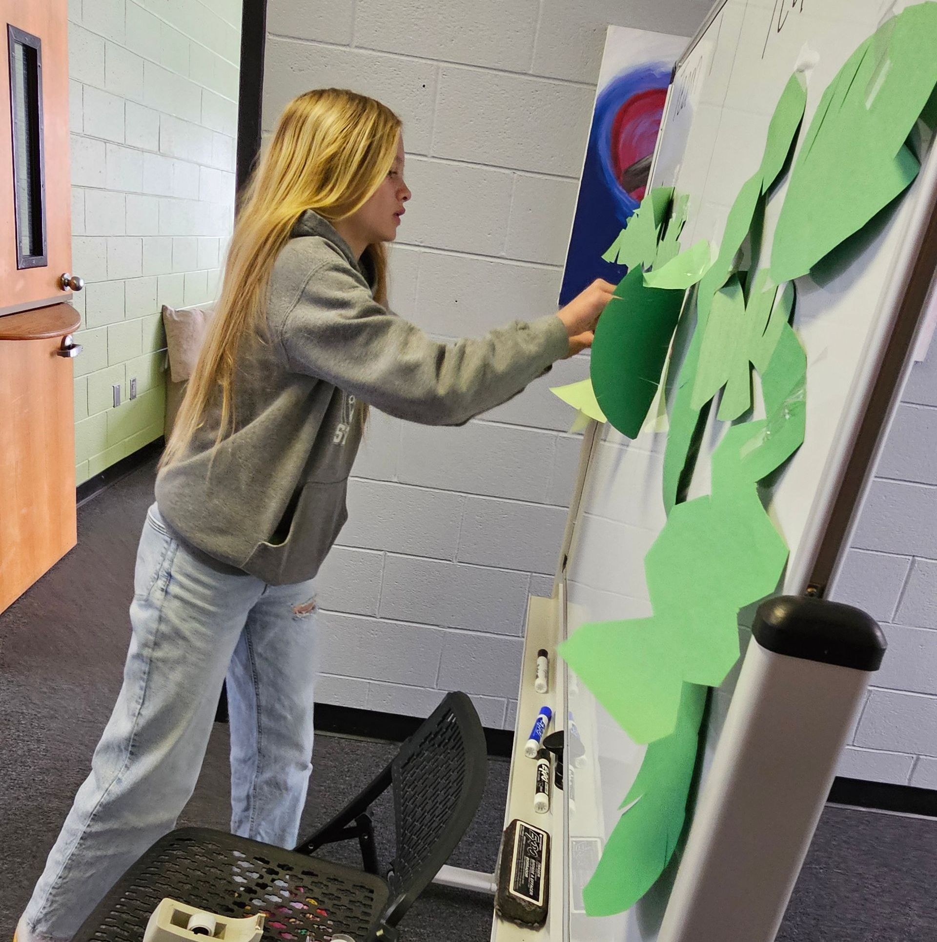 A girl is standing in front of a white board with green leaves on it