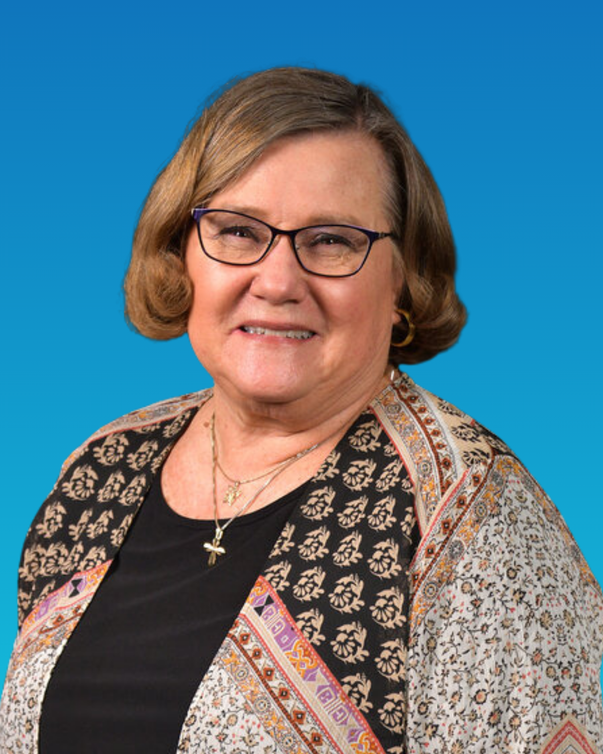 A woman wearing glasses and a necklace is smiling in front of a blue background