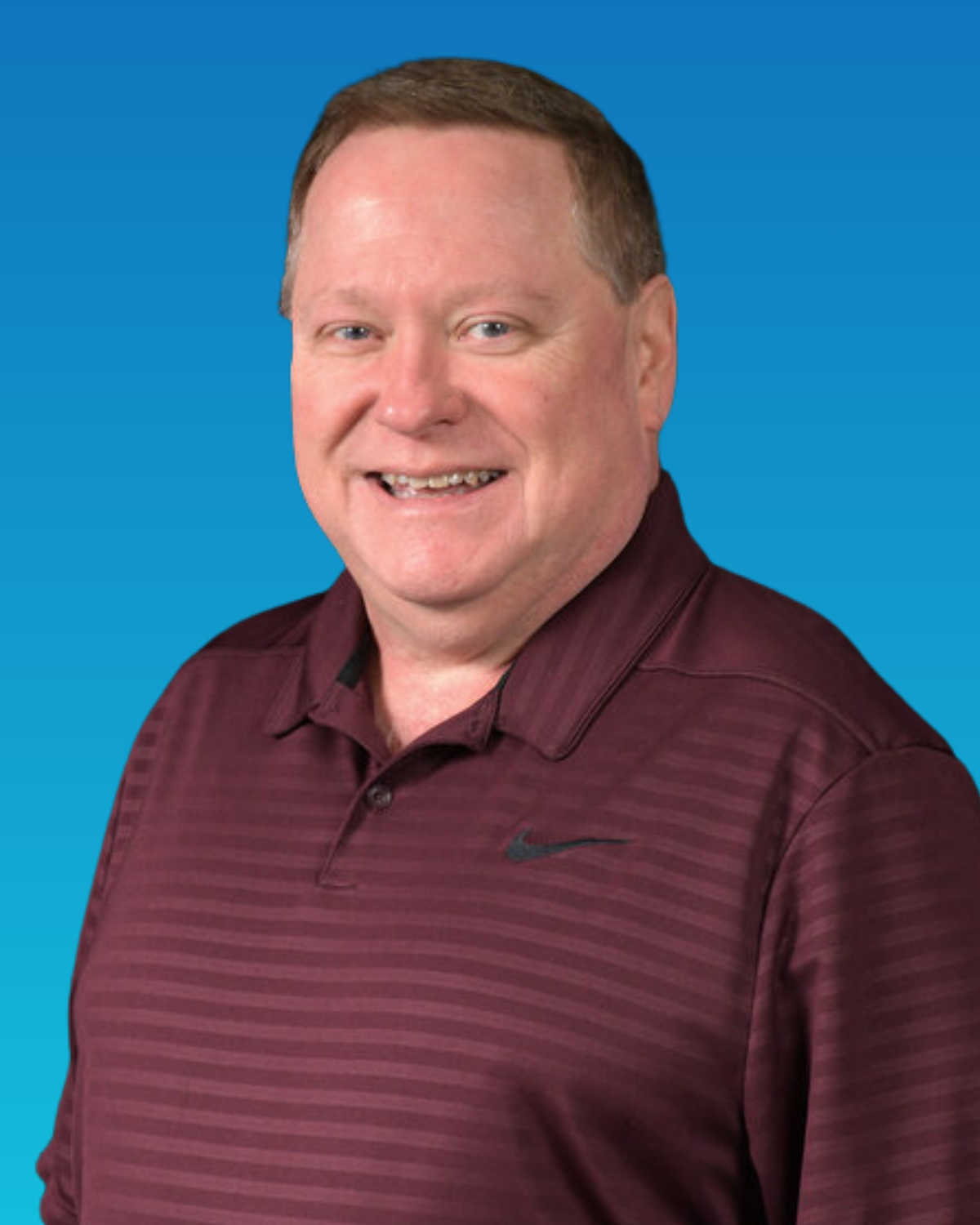 A man in a maroon striped shirt is smiling in front of a blue background.