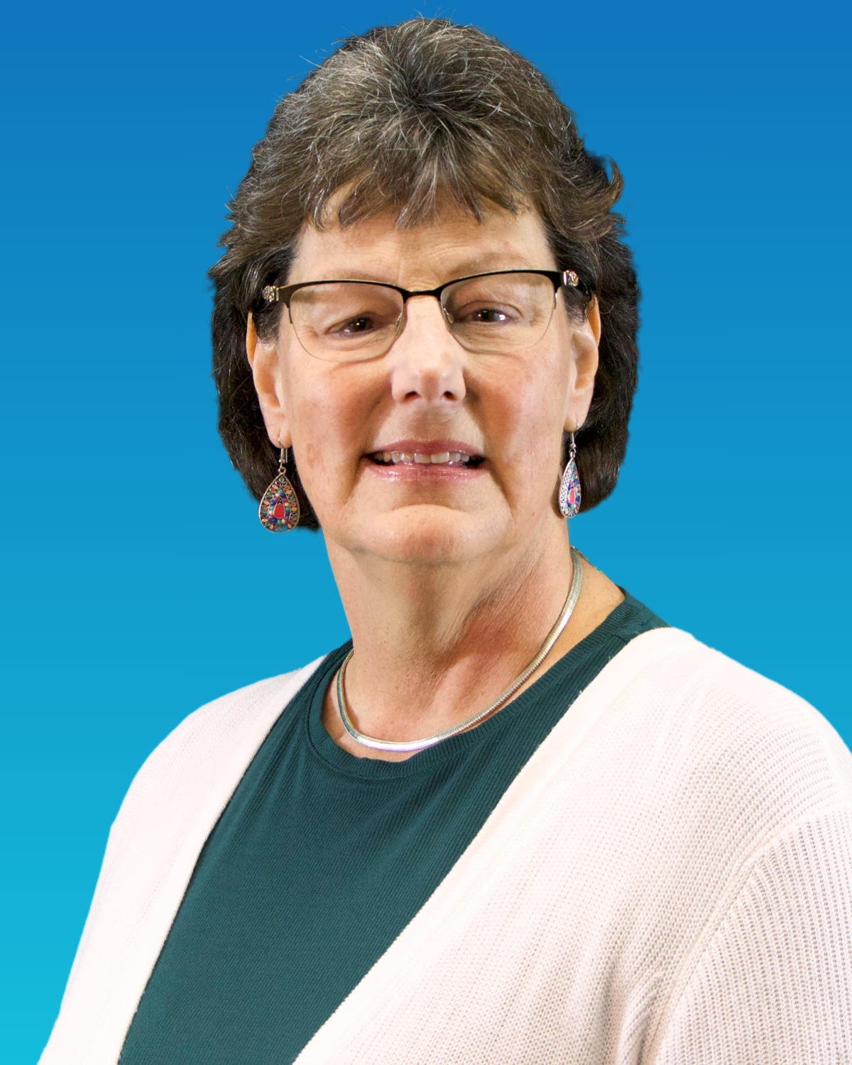 A woman wearing glasses and earrings is smiling in front of a blue background.