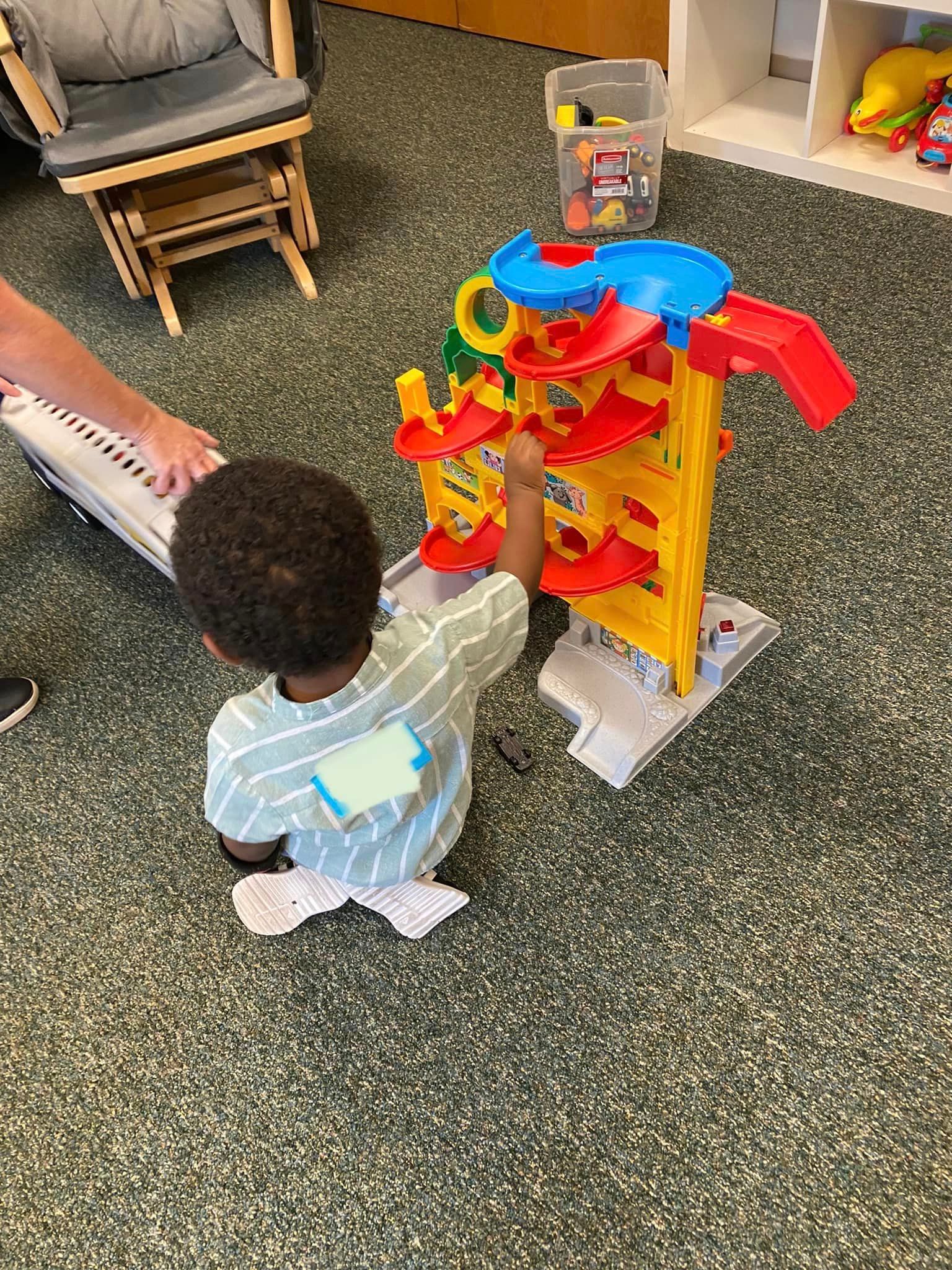 A little boy is playing with a toy car track in a room.