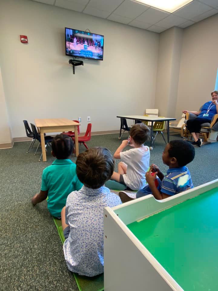 A group of children are sitting on the floor watching a tv.