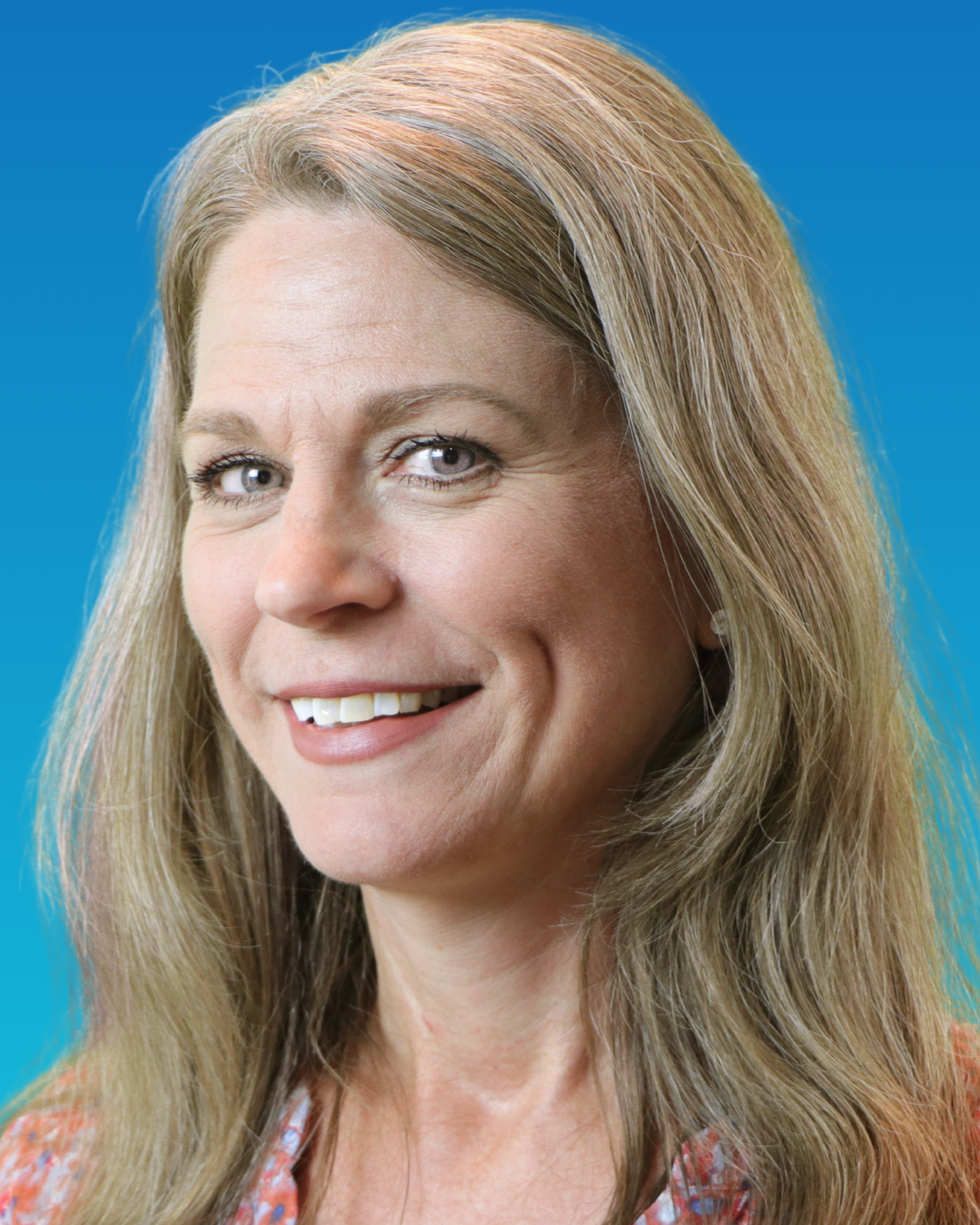 A woman in a blue sweater is smiling in front of a blue background.
