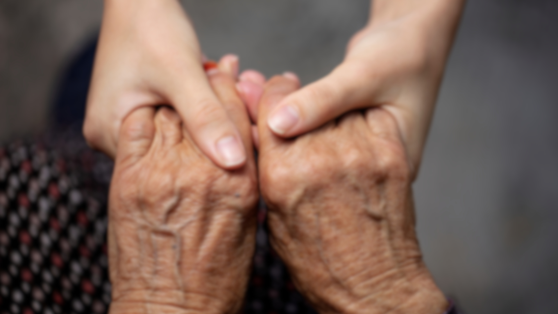 A young woman is holding the hands of an older woman.