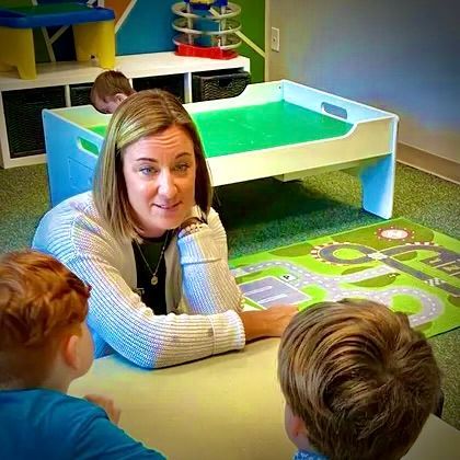 A woman is sitting at a table talking to two young boys.