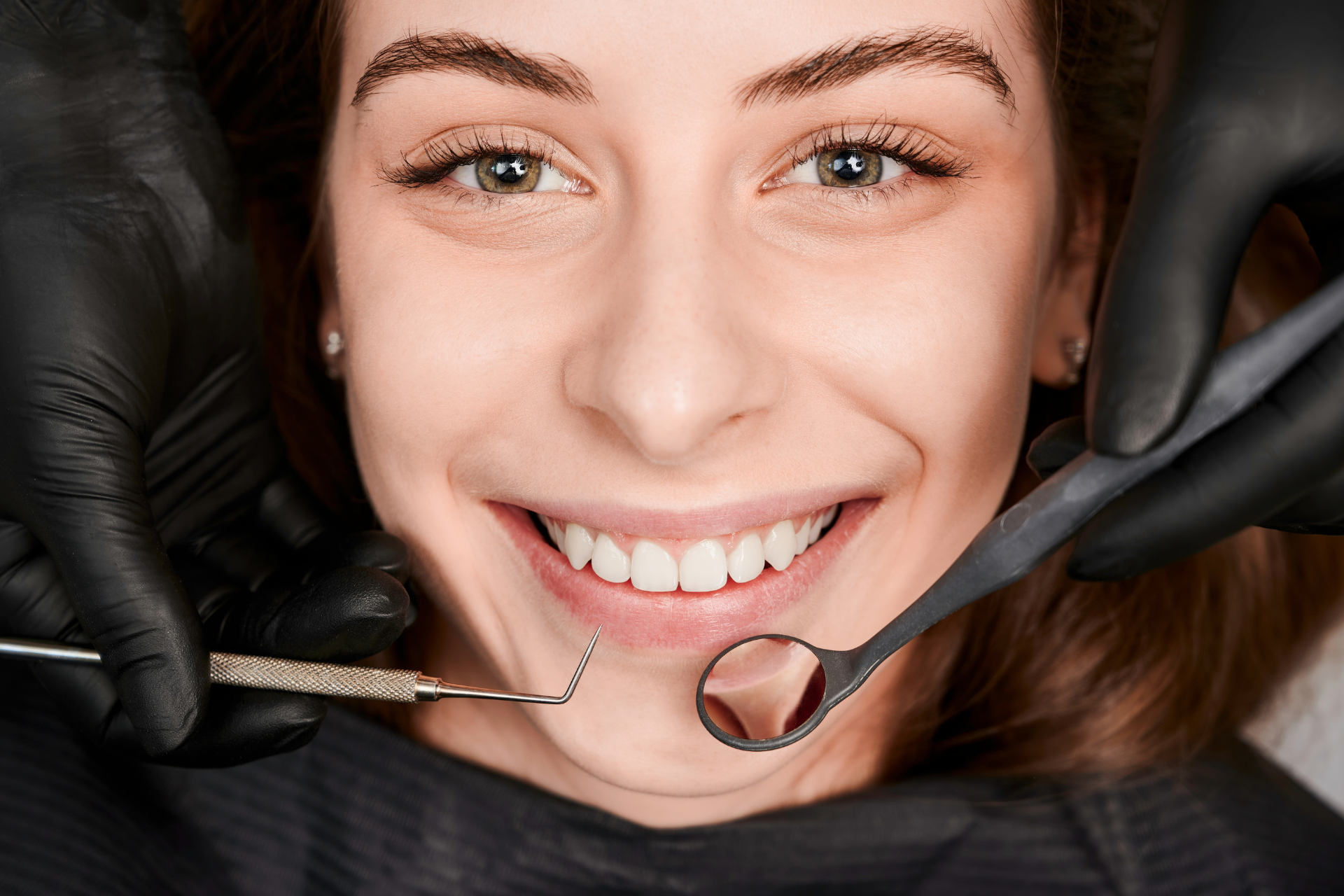 Woman smiling in a dentist chair, looking at a person holding a clipboard, dental tools nearby.