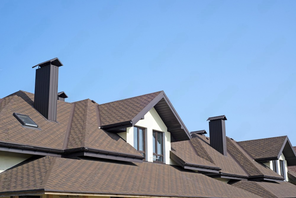 A row of houses with brown roofs and chimneys against a blue sky.