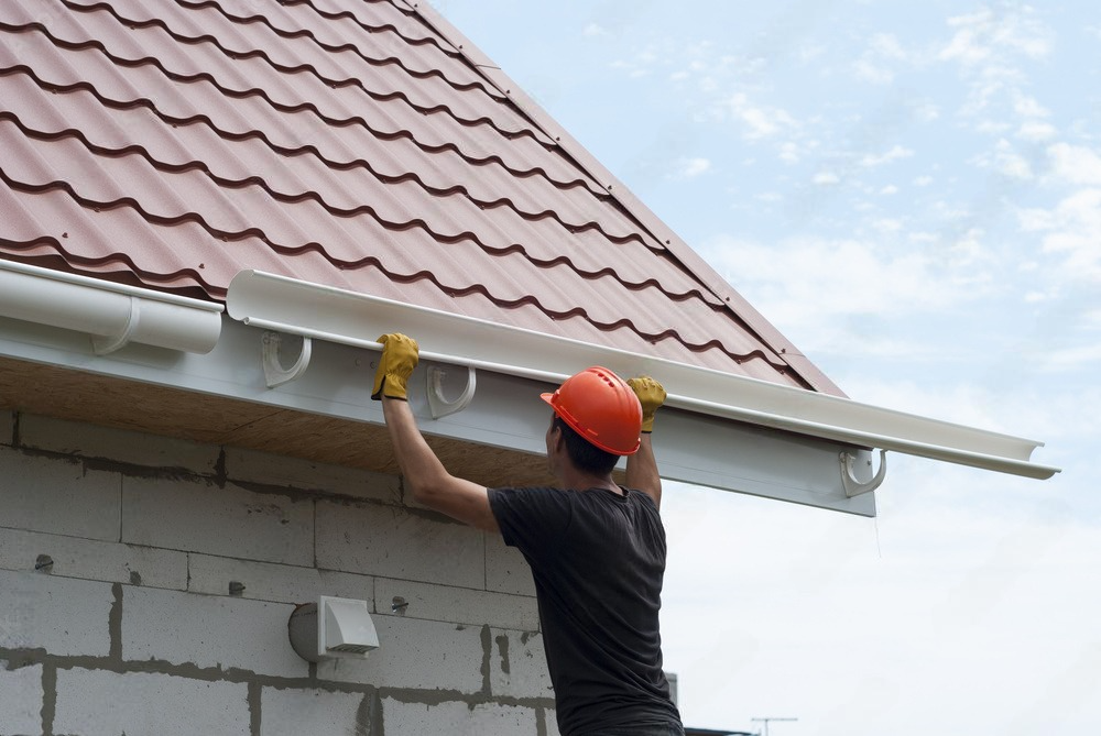 A man is installing a gutter on the side of a house.