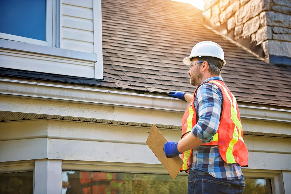 A man wearing a hard hat and safety vest is inspecting the roof of a house.