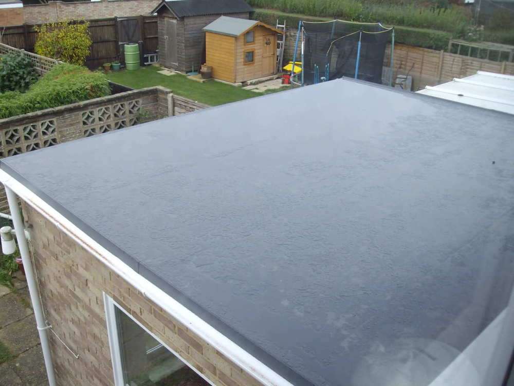 The roof of a house with a black roof and a shed in the background.