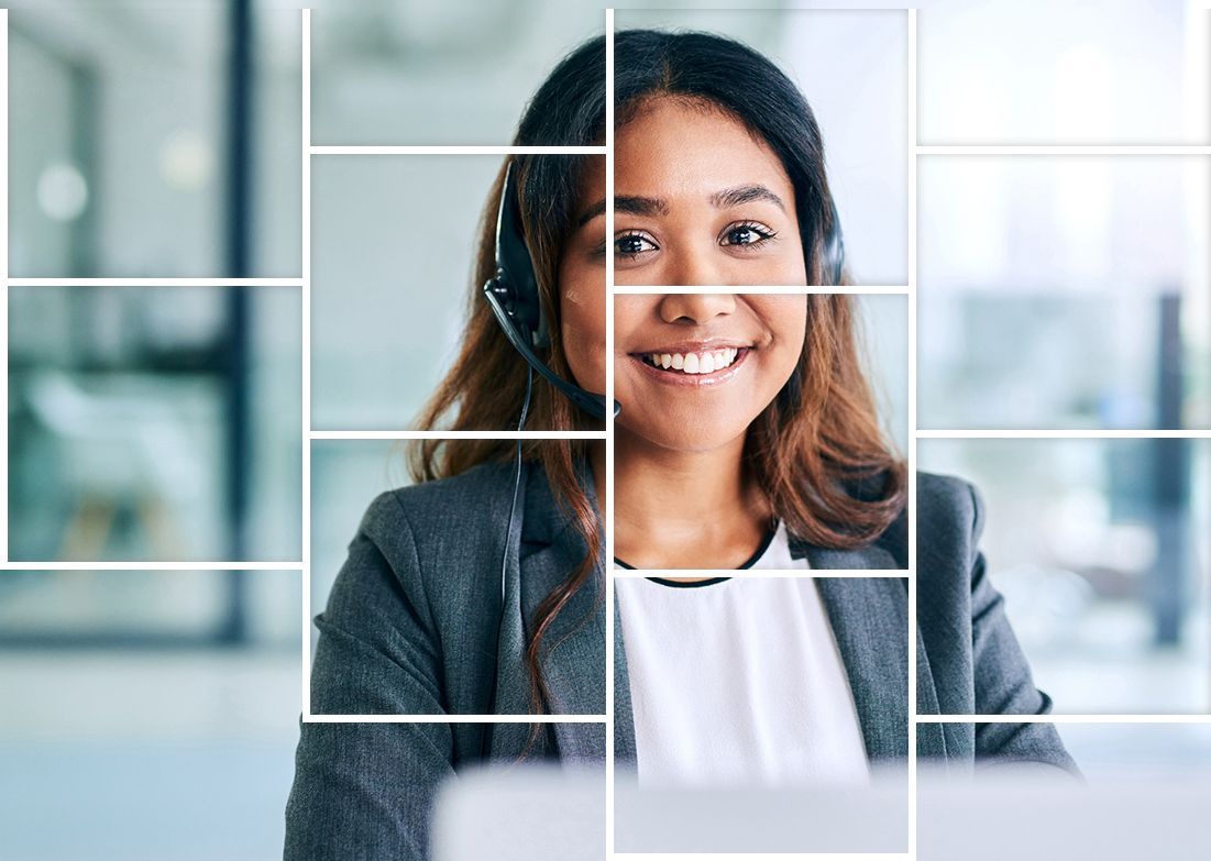 A woman wearing a headset is smiling while sitting at a desk in front of a computer.