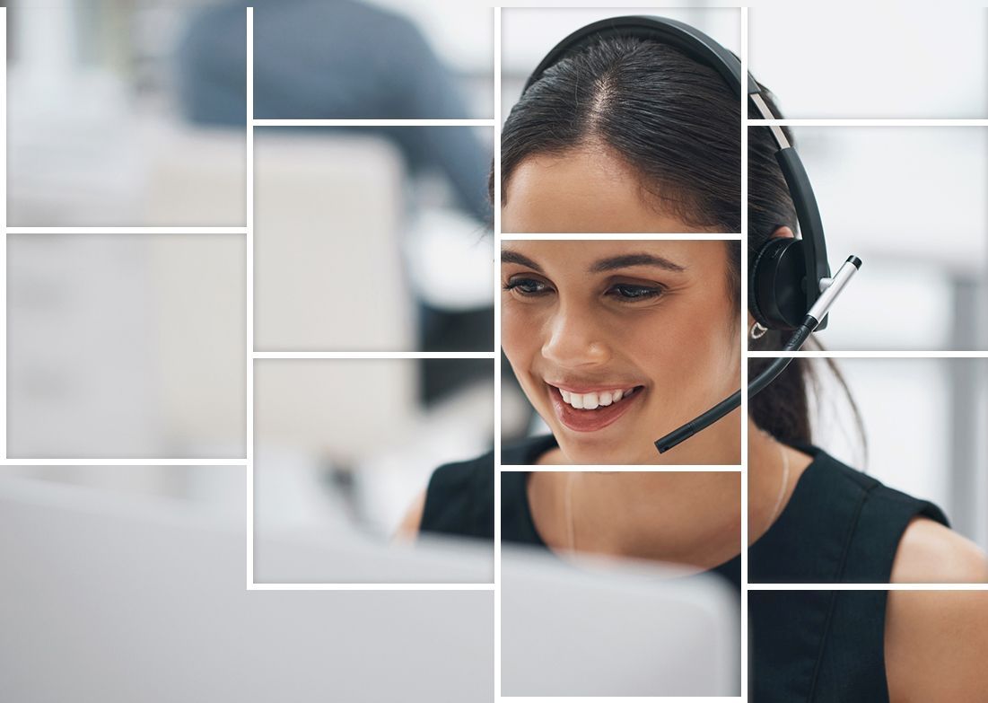 A woman wearing a headset is smiling while sitting in front of a computer.