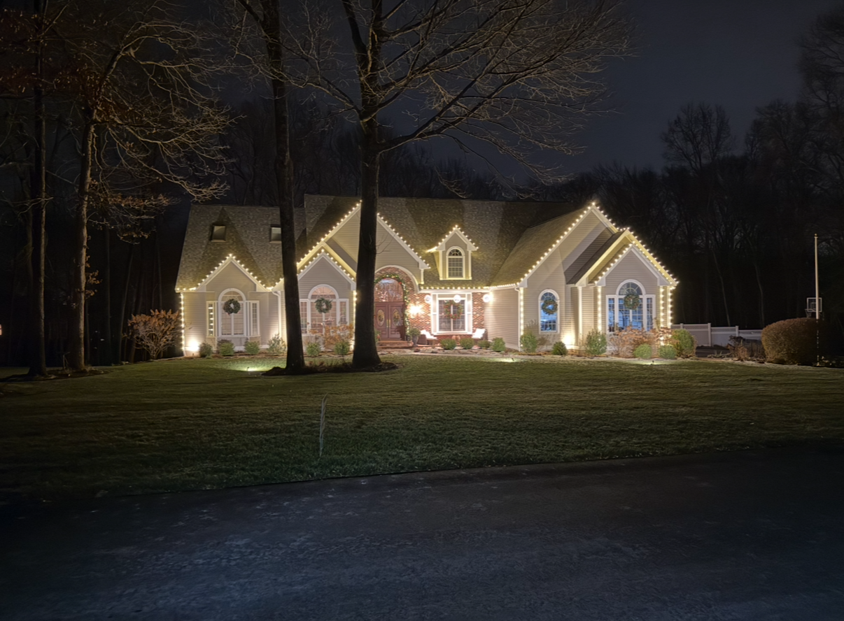 A house at night, decorated with yellow Christmas lights along the roof and windows.