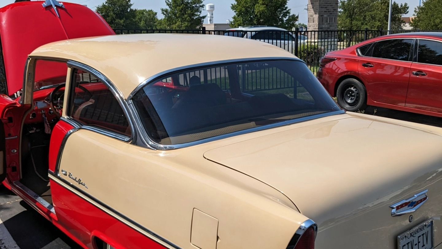 A red and white car with the hood up is parked next to a red car.