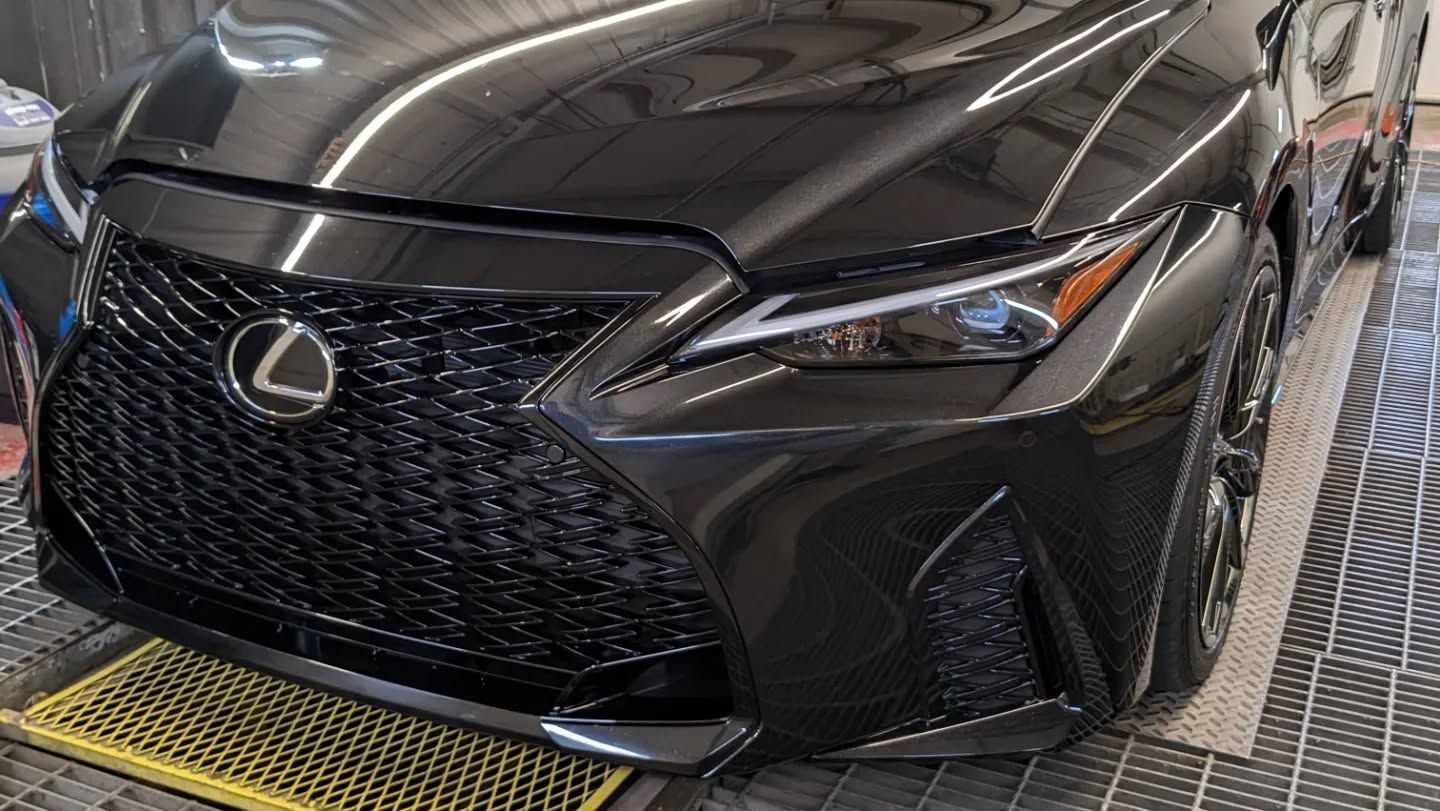 A black lexus is parked on a yellow mat in a garage.