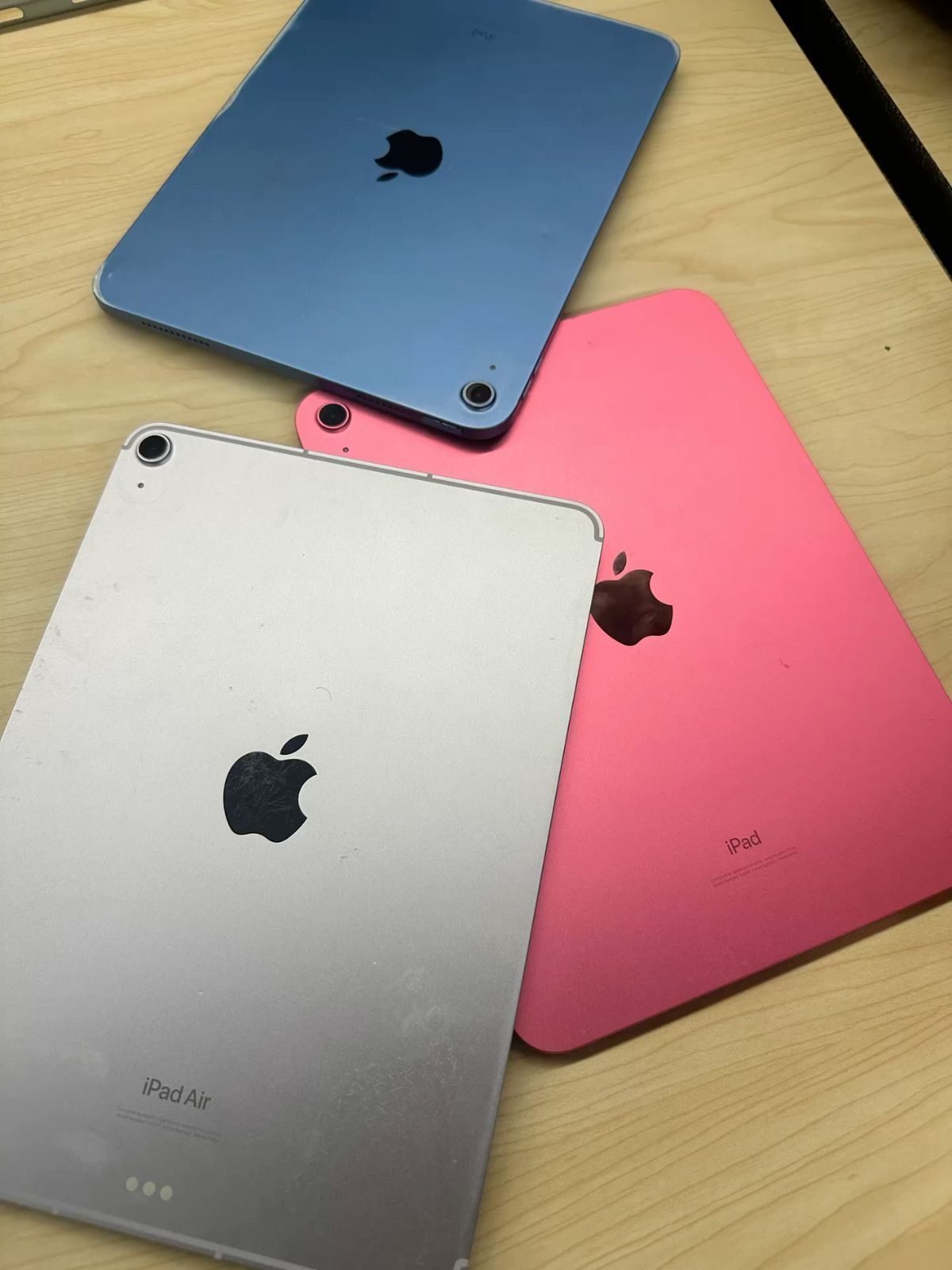 Tres iPads en azul, rosa y plata sobre una superficie de madera, mostrando el logotipo de Apple.